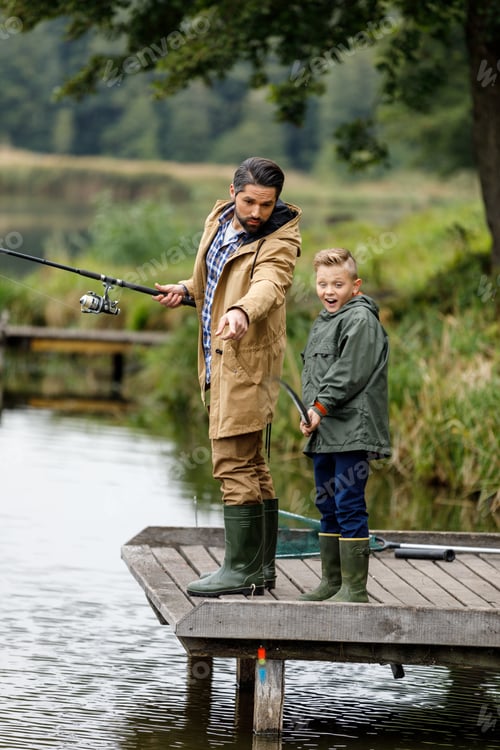 Preview: father and son fishing together with rods on wooden pier at lake