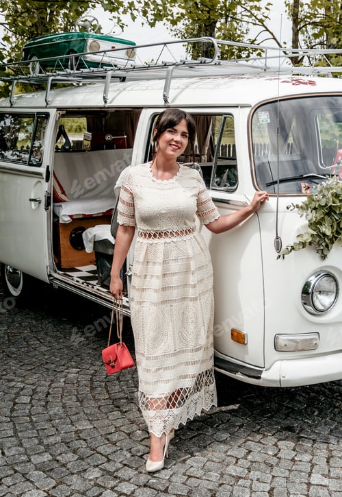 Preview: Beautiful young woman in evening dress posing for photo in front of retro vintage van.