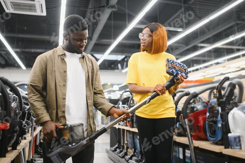 Preview: African american couple crouching and looking at vacuum cleaner they want to buy.
