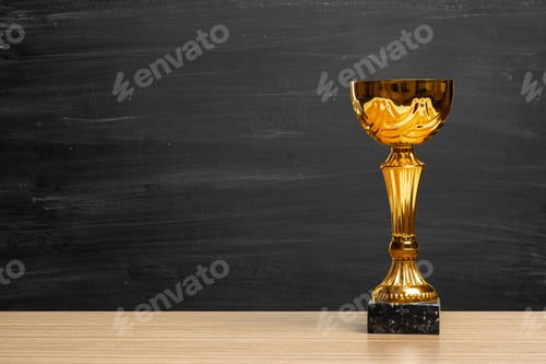 Preview: Golden trophy on a wooden table with a black chalkboard in the background