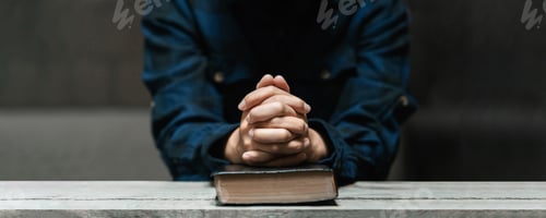 Preview: Woman hands sitting and praying with old bible in darkness on long wooden table Divine love concept