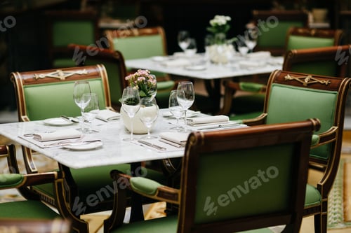 Preview: Table served with luxury glasses, cutlery, flowers, green chairs around in cozy restaurant