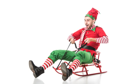 Preview: excited man in christmas elf costume riding sleigh isolated on white background