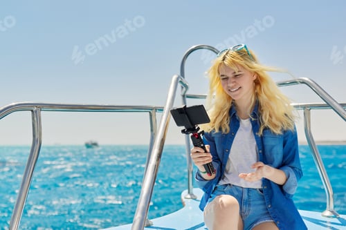 Preview: Young woman recording stream on smartphone sitting on board of yacht in sea