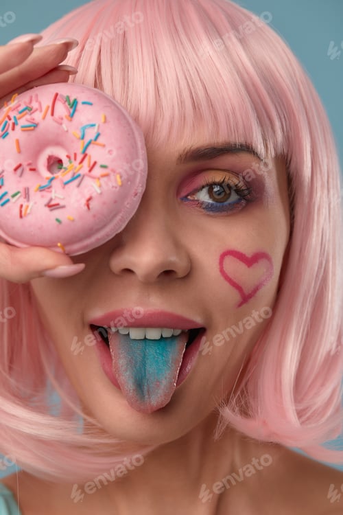 Preview: Portrait of a fashionable girl in a pink wig and with a pink donut in her hands keeps to the eye
