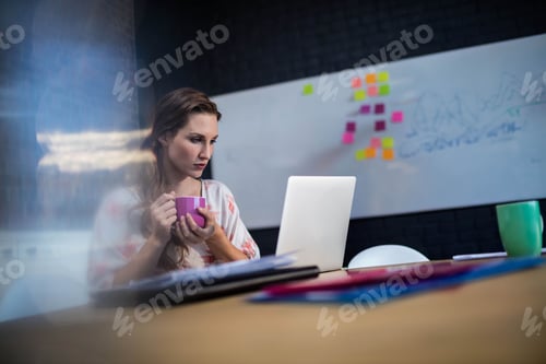 Preview: Woman holding purple mug and typing on laptop at modern office wooden table with sticky notes