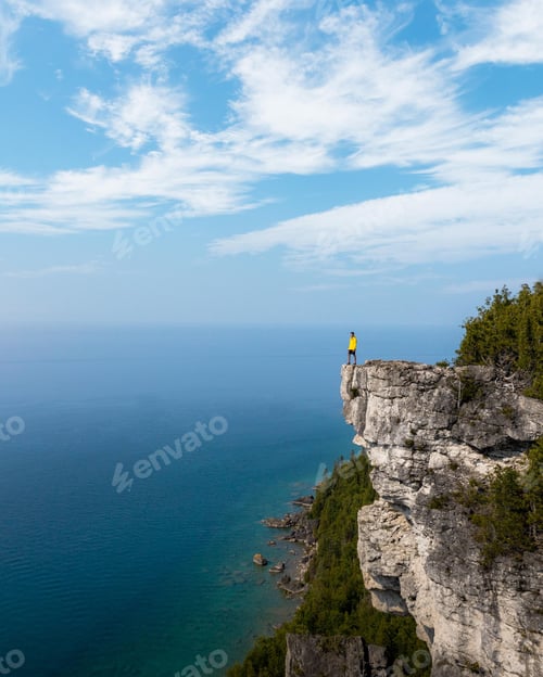 Preview: Vertical aerial shot of a man on the peak of the mountain looking at the sea