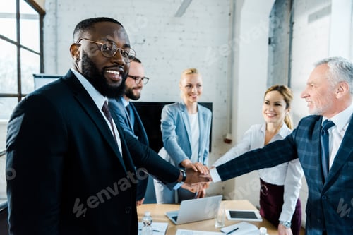 Preview: cheerful african american man looking at camera while putting hands together with coworkers