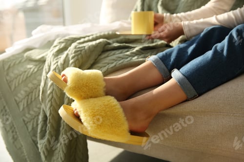 Preview: Woman with cup of drink wearing soft comfortable slippers at home, closeup