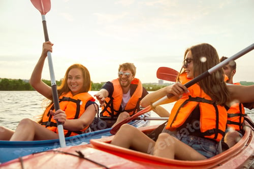 Preview: Happy friends kayaking on river with sunset on the background