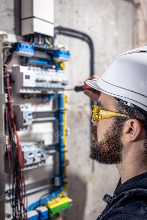 Preview: A male electrician works in a switchboard with an electrical connecting cable.