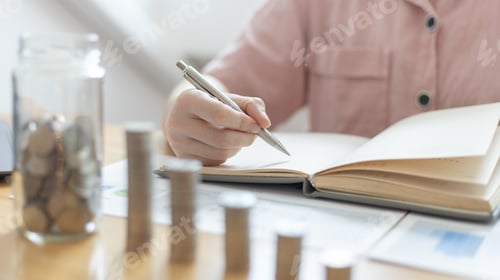 Woman Writing in Notebook with Coins and Charts