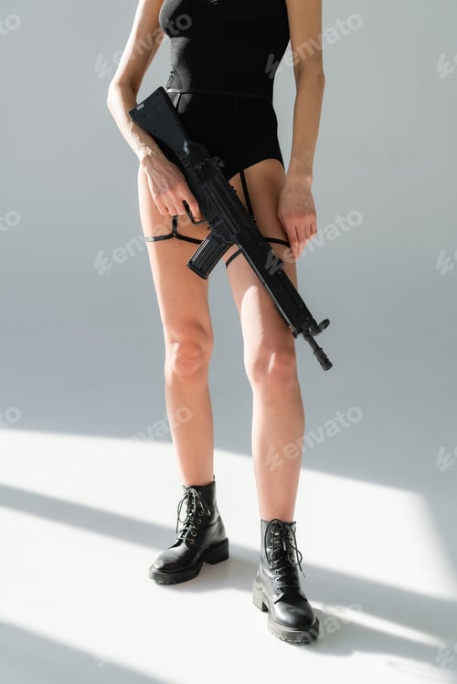 Preview: cropped view of woman in leather boots holding rifle on gray background with shadows