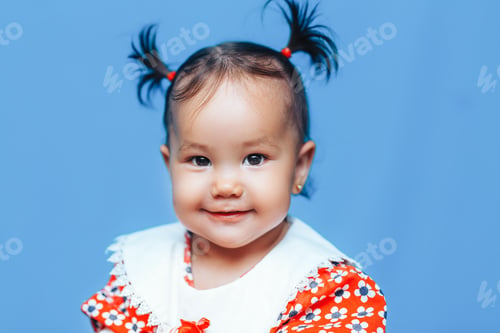 Preview: Cute one year old mixed race Asian Caucasian german girl wearing red dress smiles sweetly looking at