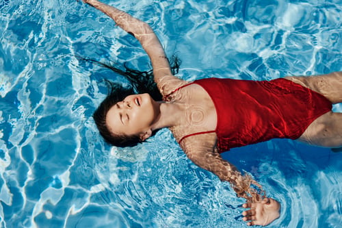 Preview: Young woman in the pool in a red swimsuit with a beautiful smile lying on the water and swimming in