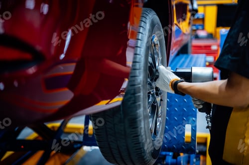 Preview: Mechanic with screwdriver repairing car wheel in workshop. Changes tire spare parts.