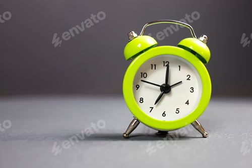 Preview: Small green alarm clock close up on gray background.