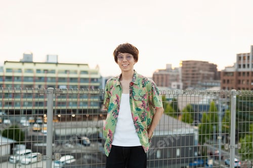 Preview: Young Japanese man standing on a rooftop in an urban setting, looking at camera.