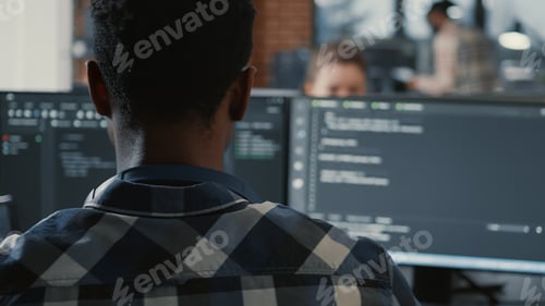 Preview: Portrait of african american programer typing on laptop sitting at desk with multiple screens