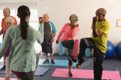 Preview: Rear view of young female trainer assisting senior people in fitness studio