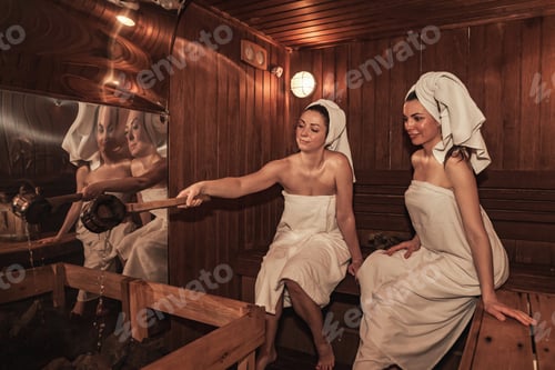 Preview: Russian bathhouse. Females with bath besoms resting on bench in spa complex. Two women relaxing and