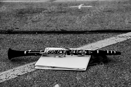 Preview: Monochromatic image of clarinet lying on a white binder in a high school parking lot.