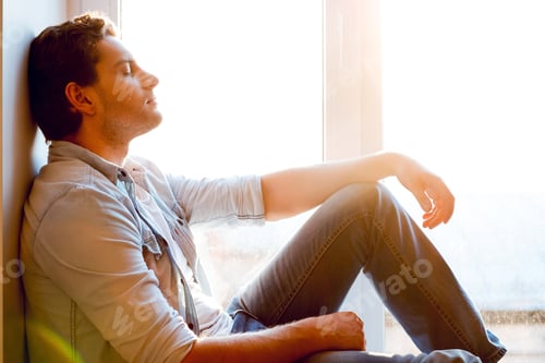 Preview: Total relaxation. Side view of handsome young man sitting at the window sill and keeping eyes closed