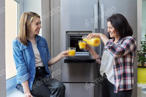 Preview: Two middle-aged women friends drinking orange juice in the kitchen