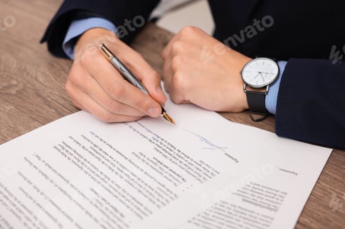 Preview: Man putting signature on document at wooden table, closeup