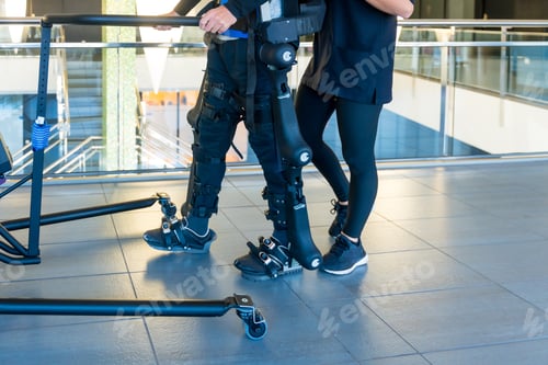 Preview: Female physiotherapy doctor helping unrecognizable disabled person with robotic skeleton to walk