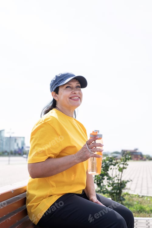Preview: Smiling senior woman drinking water after workout outdoors on the sports ground