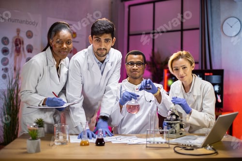 Preview: Cacasian colleague looks into microscope and laboratory technician writing results.