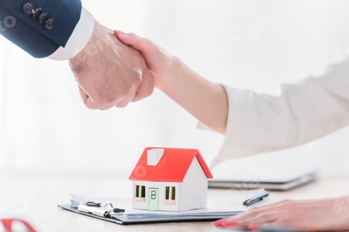 Preview: cropped shot of realtor shaking hands with client near house model on tabletop