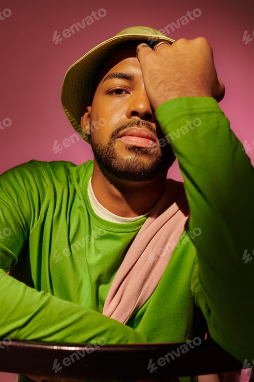 Preview: handsome young man with beard in green hat with palm on his face looking at camera, fashion concept
