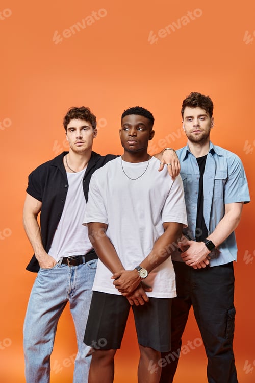 Preview: attractive fashionable diverse friends in urban attires posing on orange backdrop, fashion concept