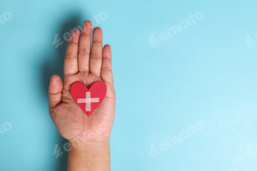 Preview: Hands holding red cross sign on heart shape over blue background