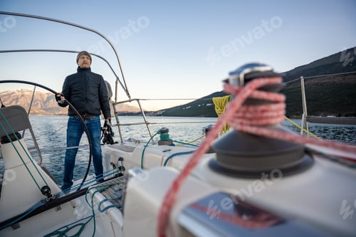 Preview: Young man captain standing at the helm and controls a sailboat during a journey by sea in winter