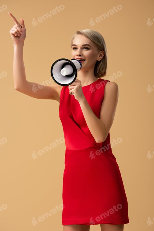 Preview: woman in red dress screaming in megaphone and pointing with finger isolated on beige