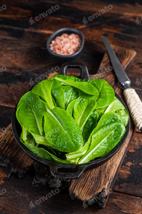 Preview: Baby romain green salad leaves in pan. Dark wooden background. Top view