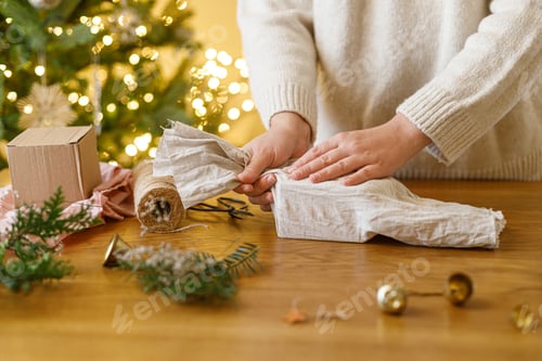 Preview: Zero waste Christmas concept. Hands wrapping stylish christmas gift in linen fabric with fir branch