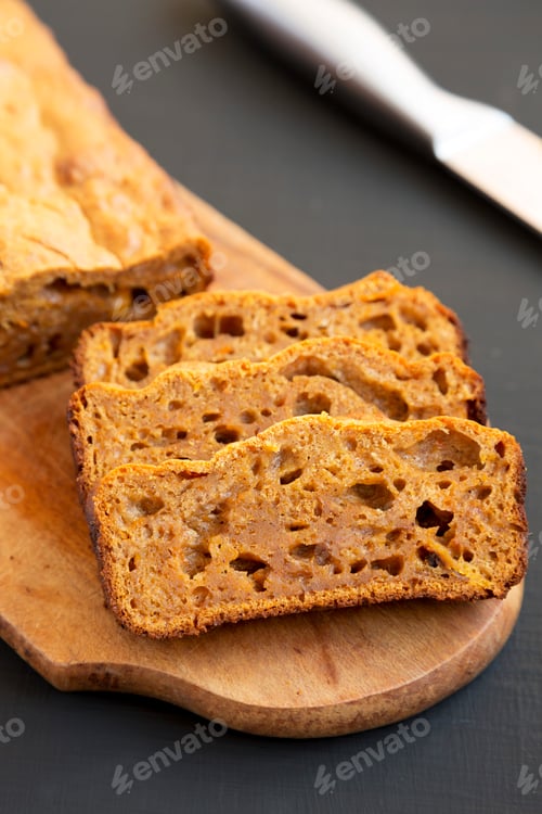 Preview: Homemade Pumpkin Loaf Bread on a rustic wooden board on a black background, low angle view.