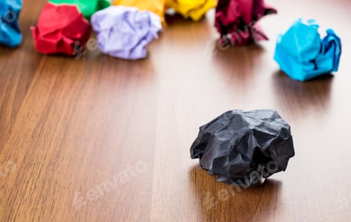Preview: Black crumpled paper ball on dark brown wood table with group of colorful crumpled paper