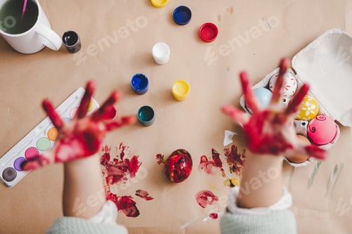 Preview: Child showing dirty hands near chicken eggs and colors at table