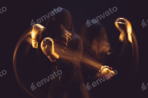 Preview: motion shot of woman in black hoodie and boxing gloves exercising isolated on black