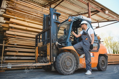 Preview: Warehouse worker stepping down from forklift near lumber stacks