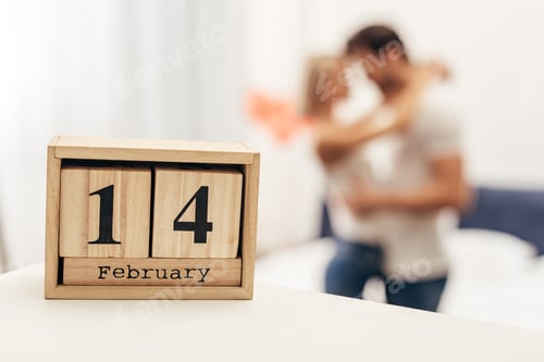 Preview: selective focus of wooden calendar with 14 february lettering and young couple on background on