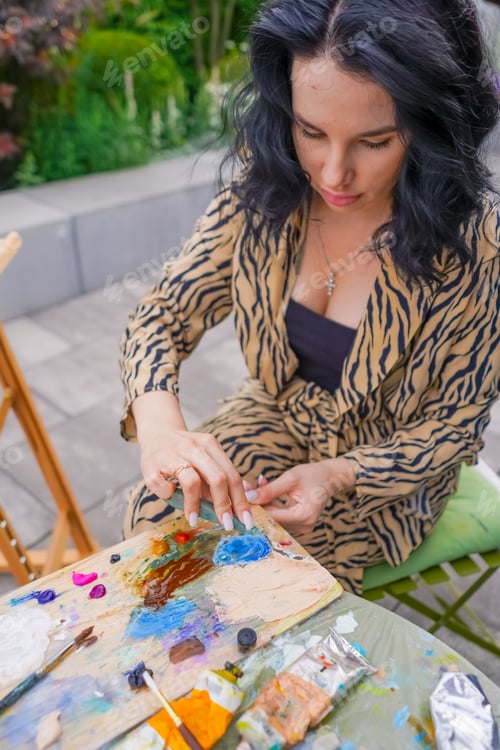 Preview: young pretty girl artist sits on a chair on the street and takes paint from the palette