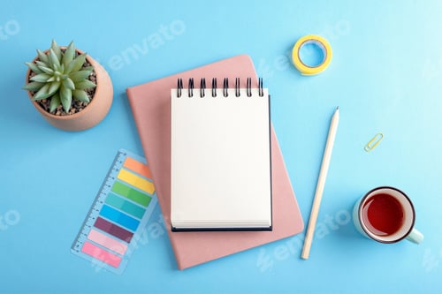Preview: Notebook with pencil, succulent plant, tea cup and color palette on blue desk.