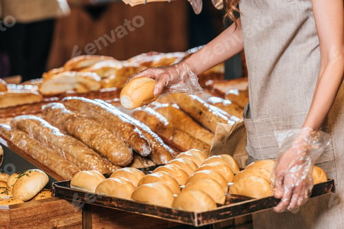 Preview: partial view of shop assistant arranging loafs of bread in shopping market