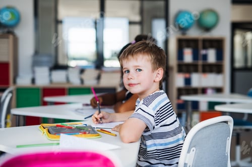 Visualização: Um pequeno estudante sentado à mesa na sala de aula, escrevendo